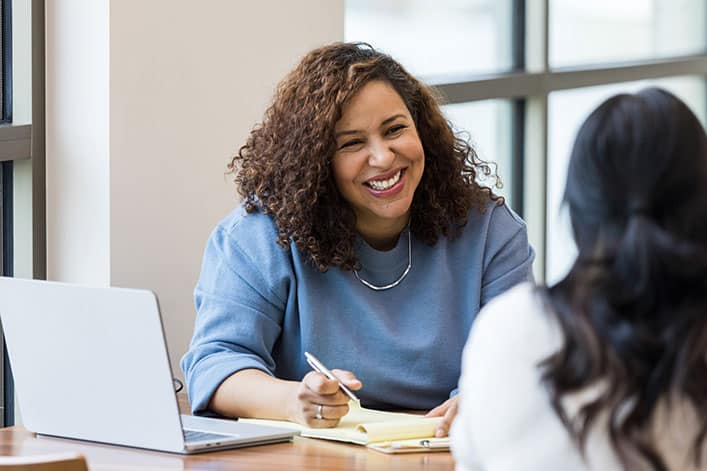 HRMgmt-GettyImages-1471886613 A smiling human resources professional interviews a potential new hire.