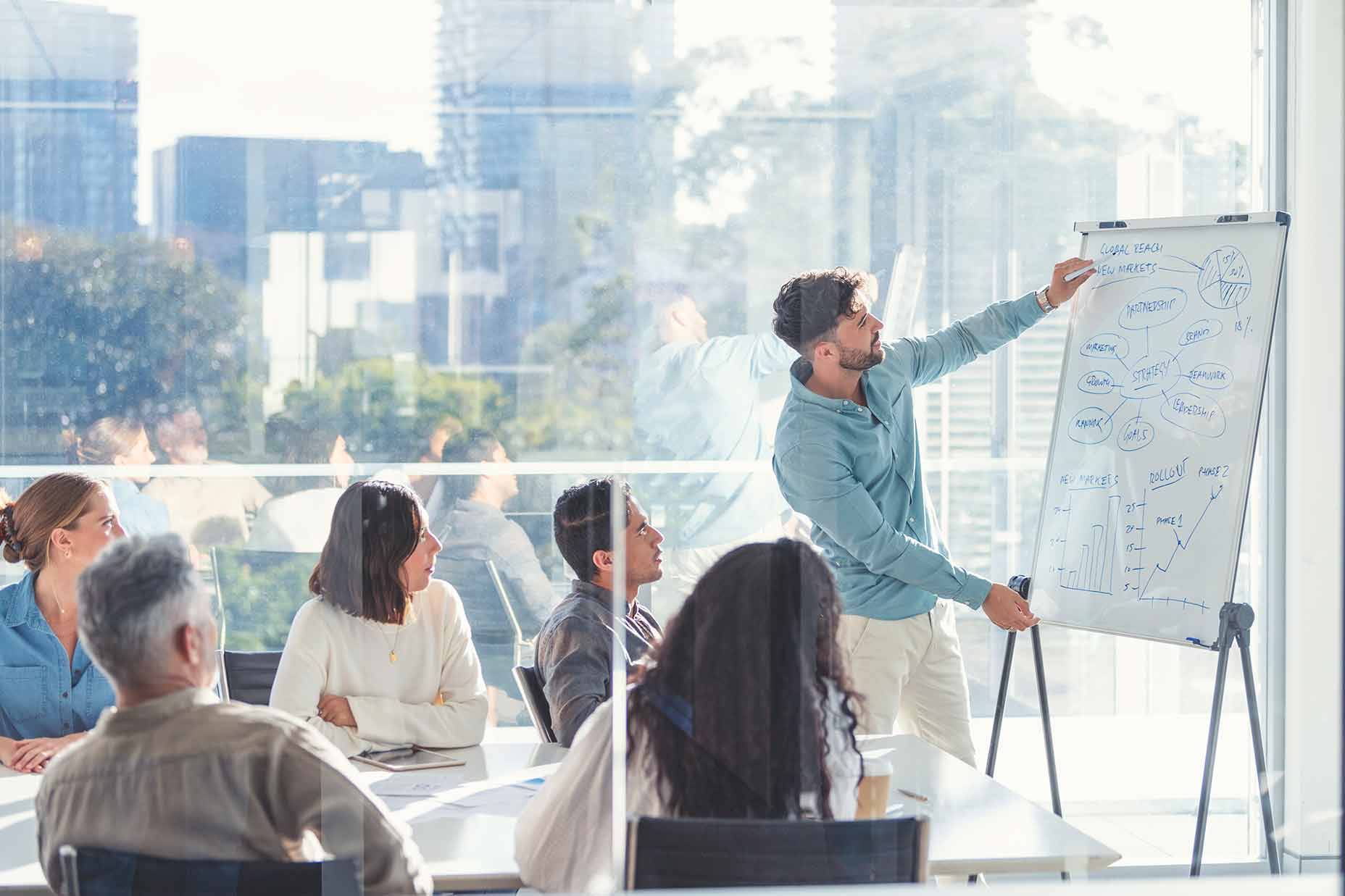 Master of Arts in Organizational Leadership Online Businessperson presents to a group of colleagues in a conference room.
